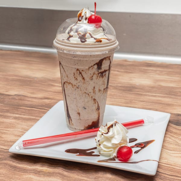 Allegro Pizza's chocolate milkshake with whipped cream, chocolate drizzle, and a cherry on a white plate.