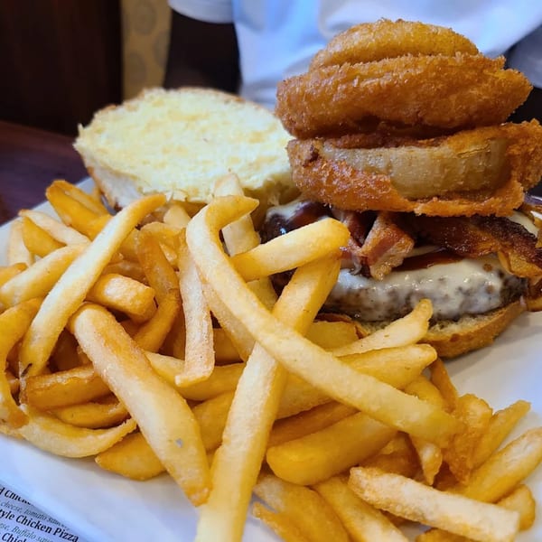 A close-up of a burger with bacon, melted cheese, and onion rings, served with a side of fries.