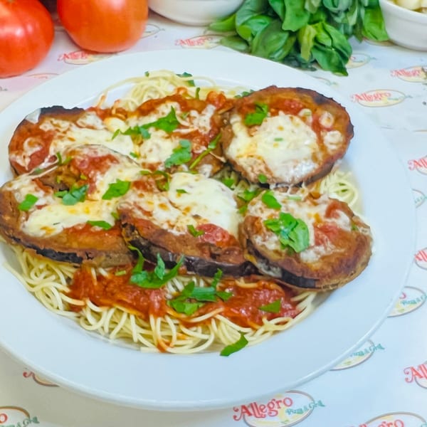 Allegro Pizza's eggplant parmesan with melted cheese and red sauce over spaghetti, garnished with parsley.