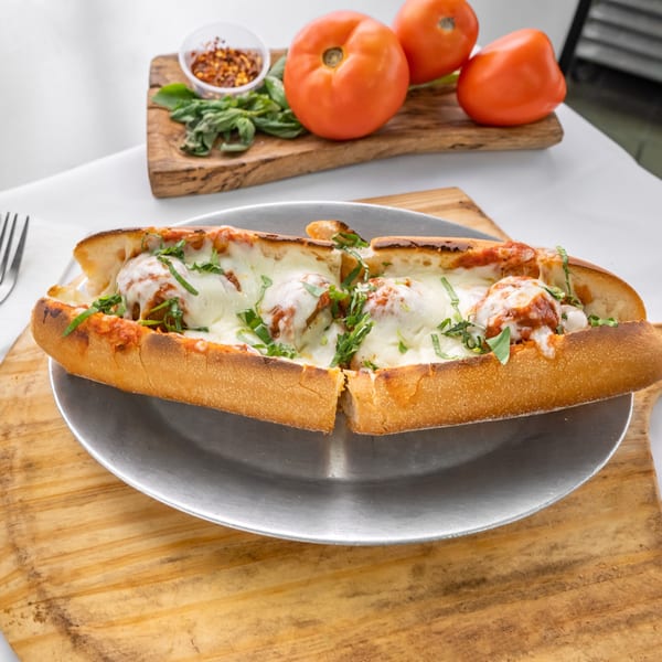 Allegro Pizza's meatball sub, cut in half, with melted cheese, sauce, and basil on a metal plate.