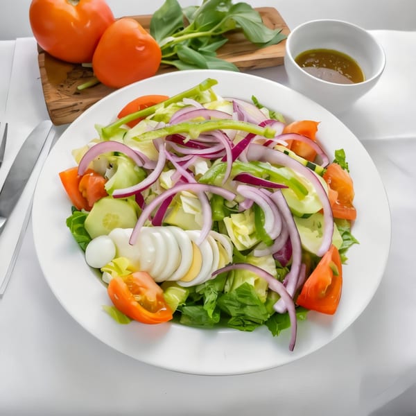 A fresh garden salad with lettuce, tomatoes, cucumbers, red onions, green peppers, and sliced hard-boiled eggs.