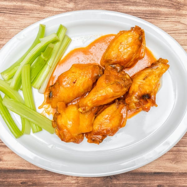 Allegro Pizza's buffalo wings and celery sticks on a white plate, against a wooden background.